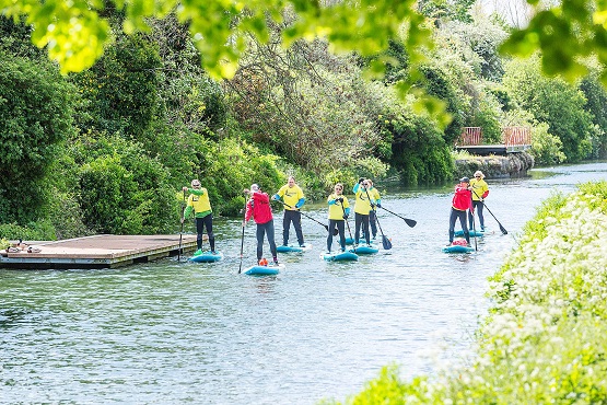 A group of stand up paddleboarders travelling down a river